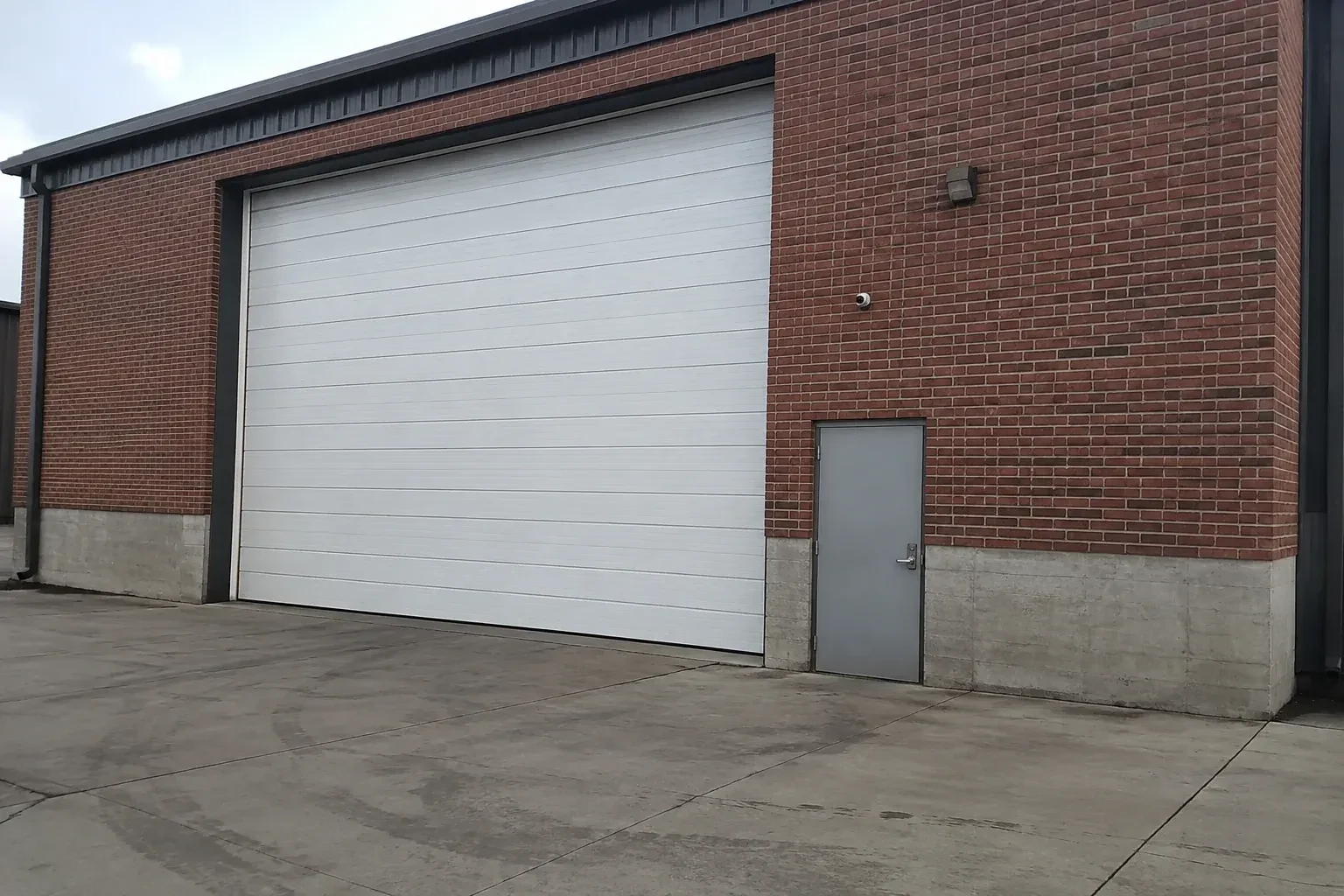 Tall closed sectional loading door beside a personnel door at a brick unit. — Commercial Sectional Door Repair, Vaughan